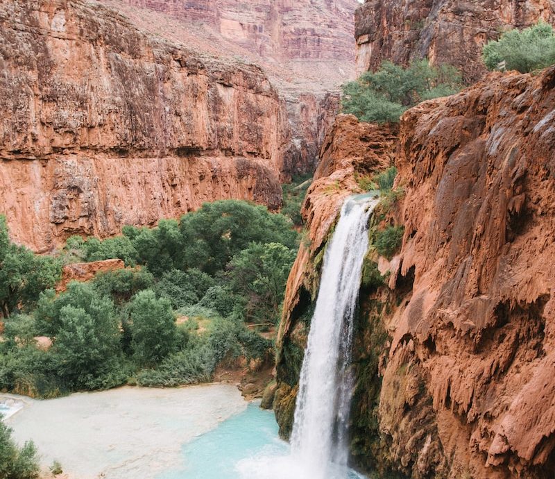 timelapse photography of waterfalls surrounded by green leafed trees and mountains